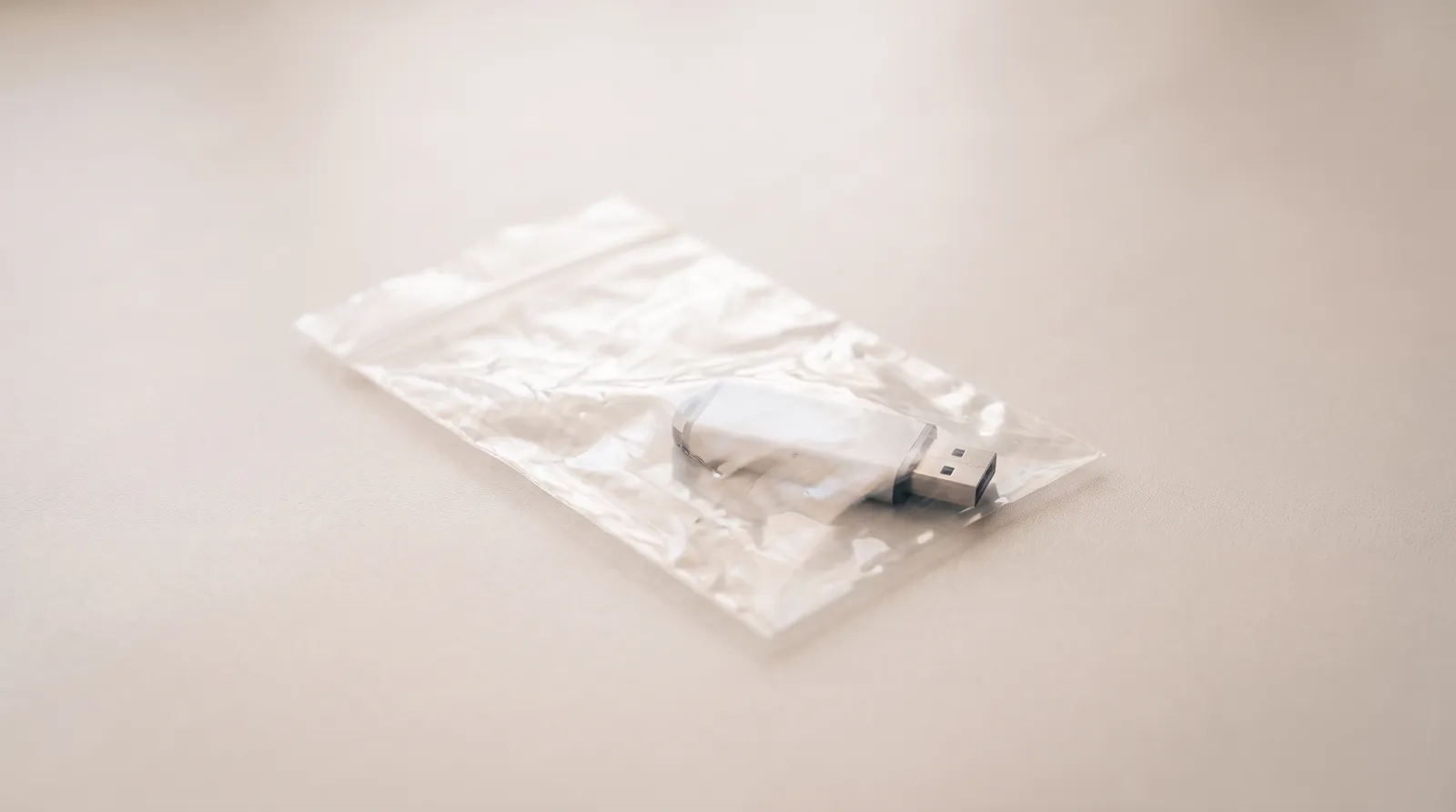 Une clé USB scellée dans un sachet plastique transparent, posée sur une table de métal sombre, éclairée par une seule lumière corail